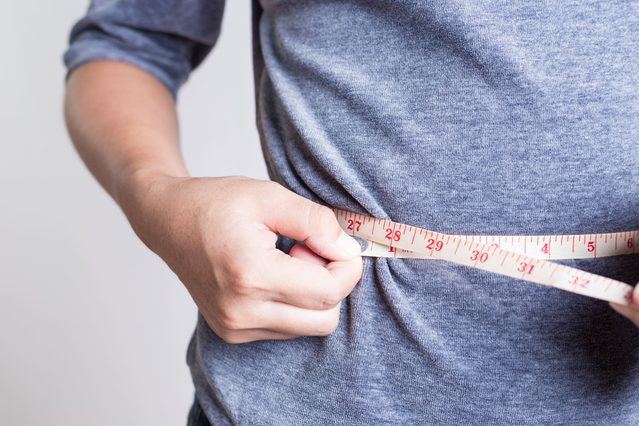 person measuring their waist with tape measure
