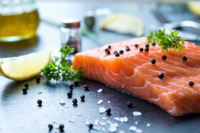 Salmon filet with parsley and capers, with a lemon wedge next to it.