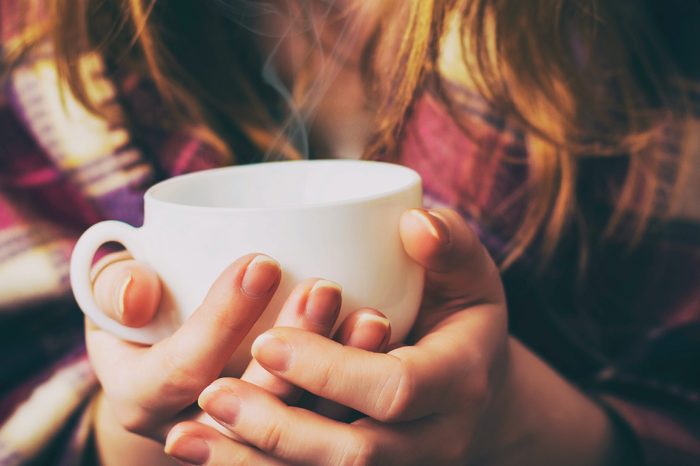 Woman wearing a plaid shirt holding a mug of tea in both hands.