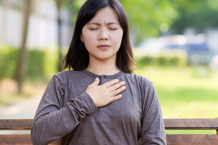 Asian woman with her eyes squeezed shut, holding her chest
