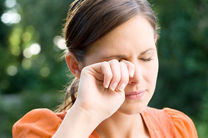 Woman standing outside wiping at her eye with her right hand.
