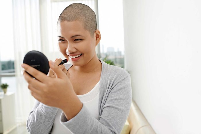 woman with shaved head applying makeup