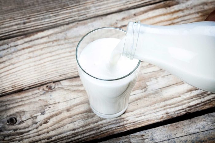 Milk from a bottle being poured into a glass, which is resting on a wooden table.