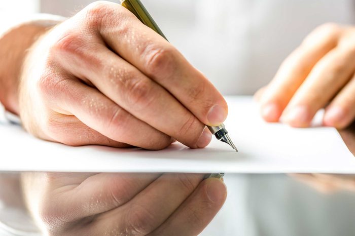 Man's hand using a pen to write on a piece of white paper.