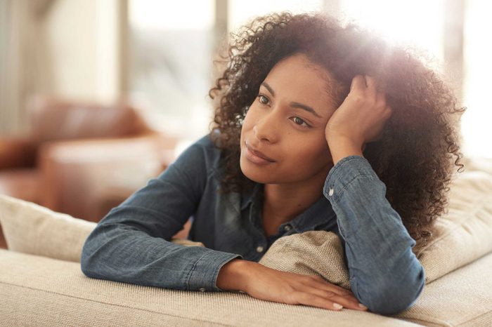 A woman in a denim shirt leaning on the back of a couch.