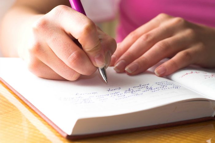 Woman in a pink top writing in a journal with a pen.