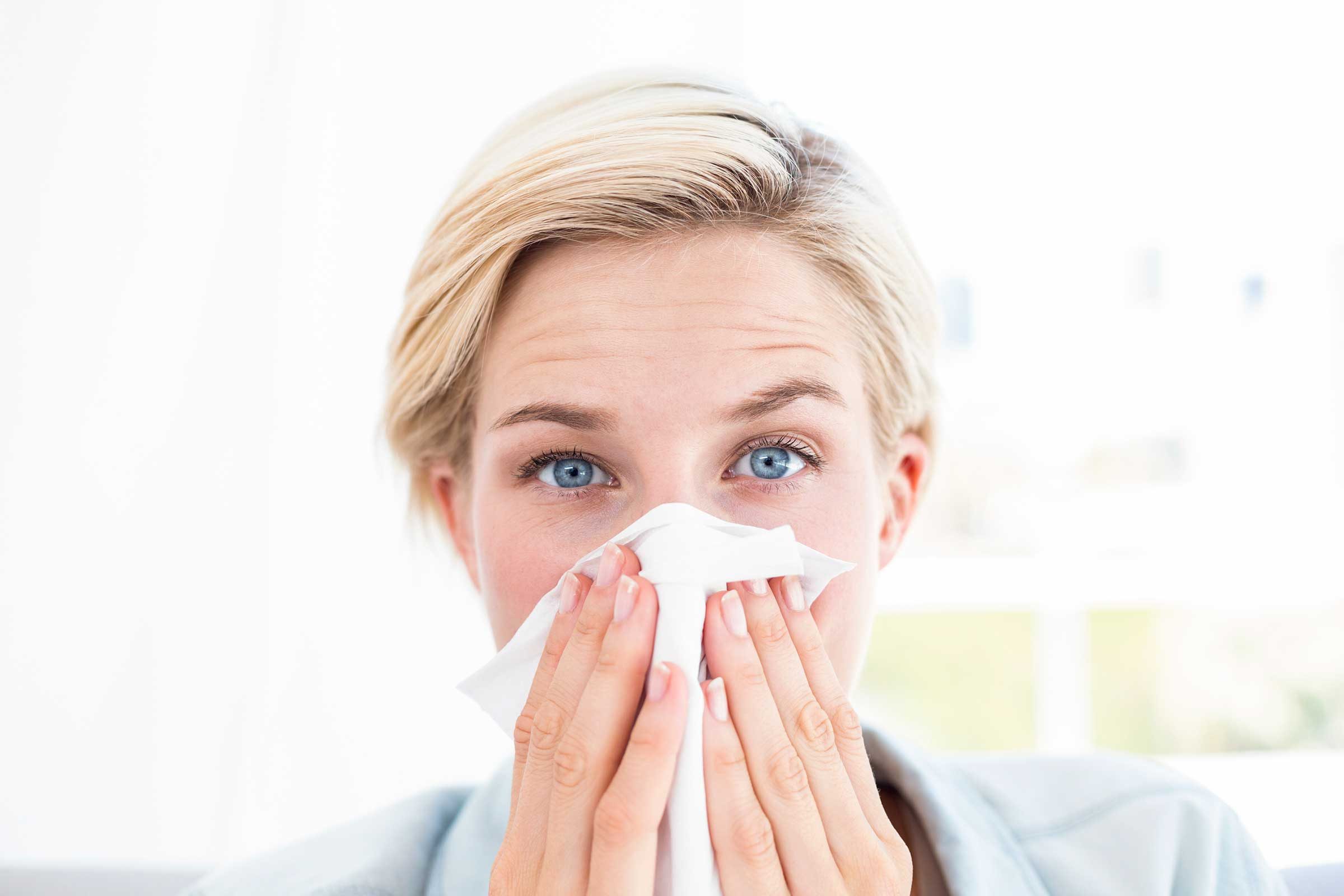 Woman with bright blue eyes blowing her nose.