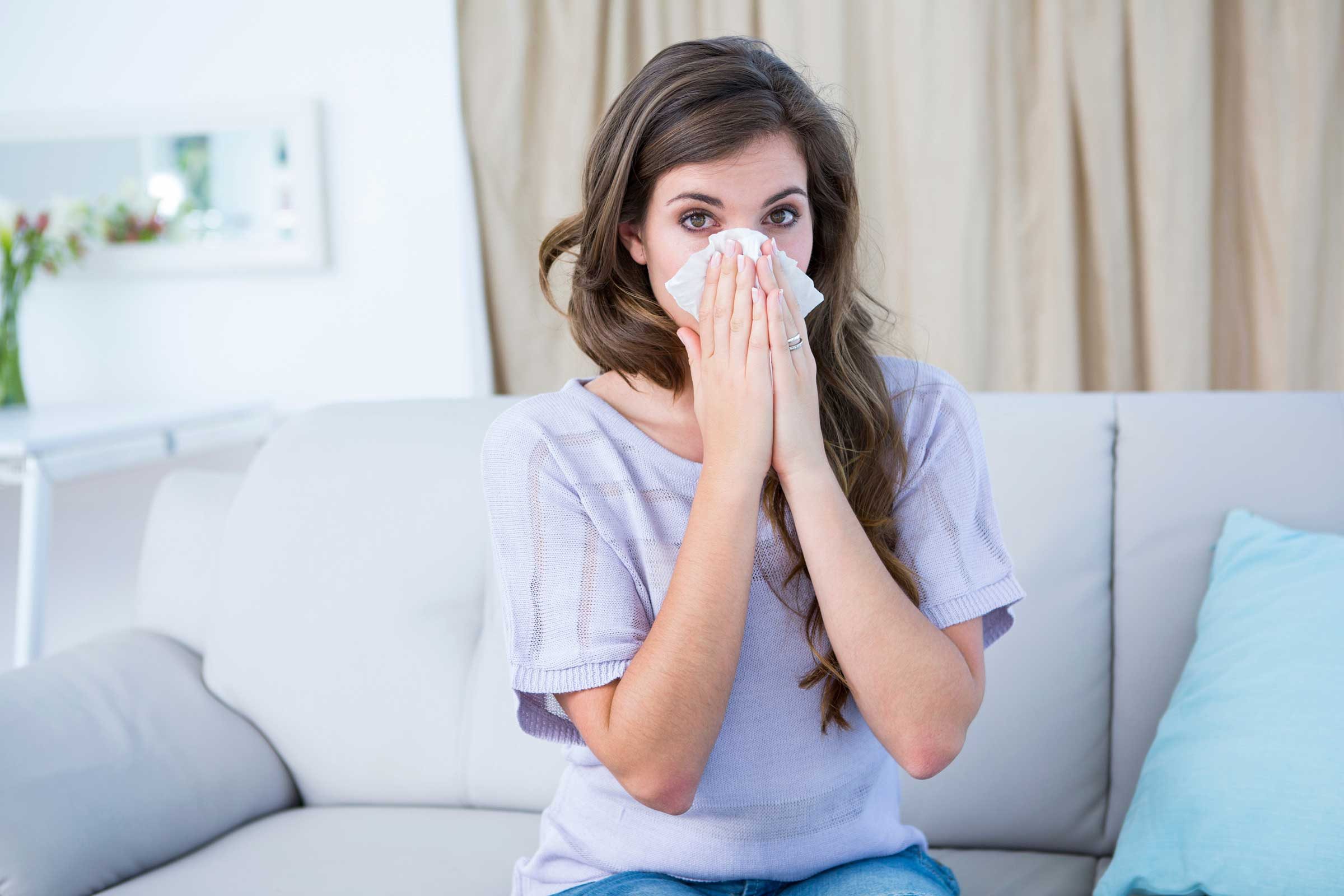 Woman sitting on the couch blowing her nose.