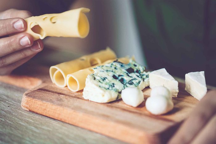 Hand holding cheese next to a cheese board