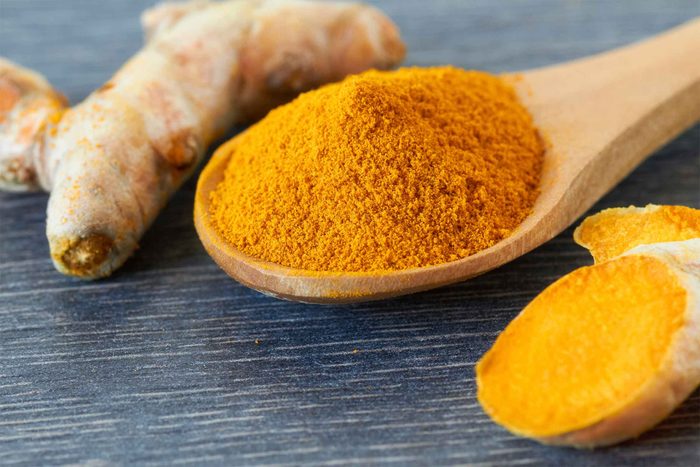 Whole turmeric root and ground turmeric in a wooden spoon.