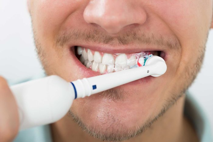 man brushing teeth with electric toothbrush
