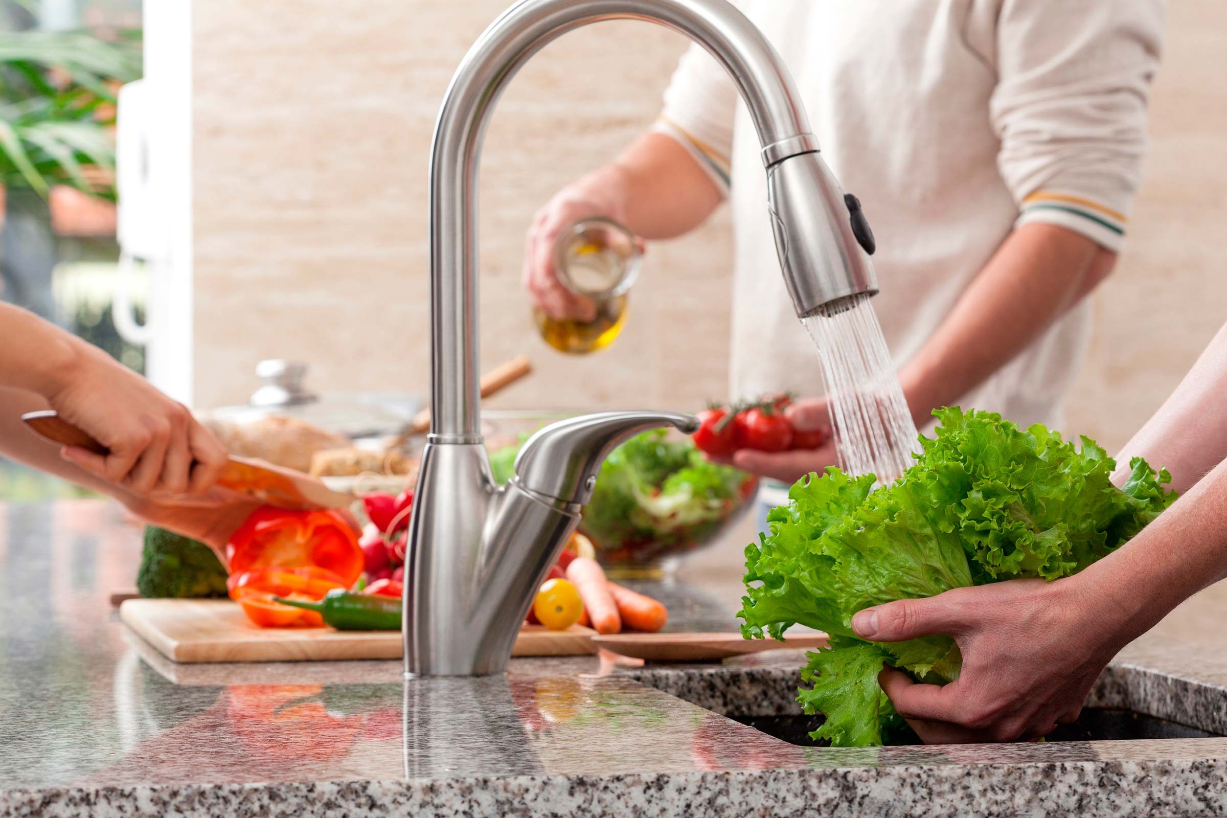 People cutting and washing vegetables for a salad.