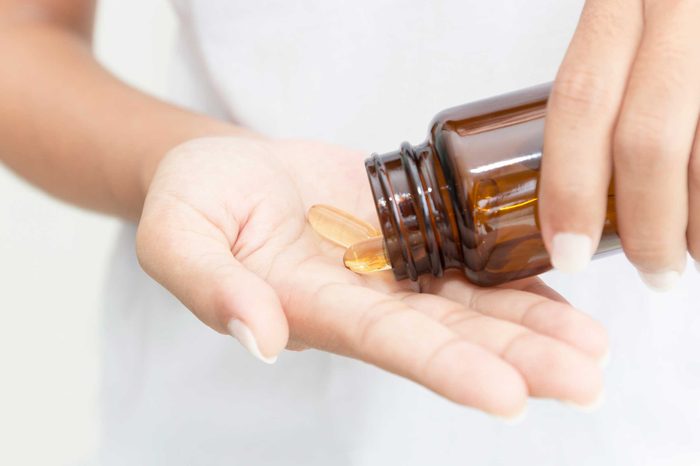 Woman pouring capsules into her hand out of a bottle.