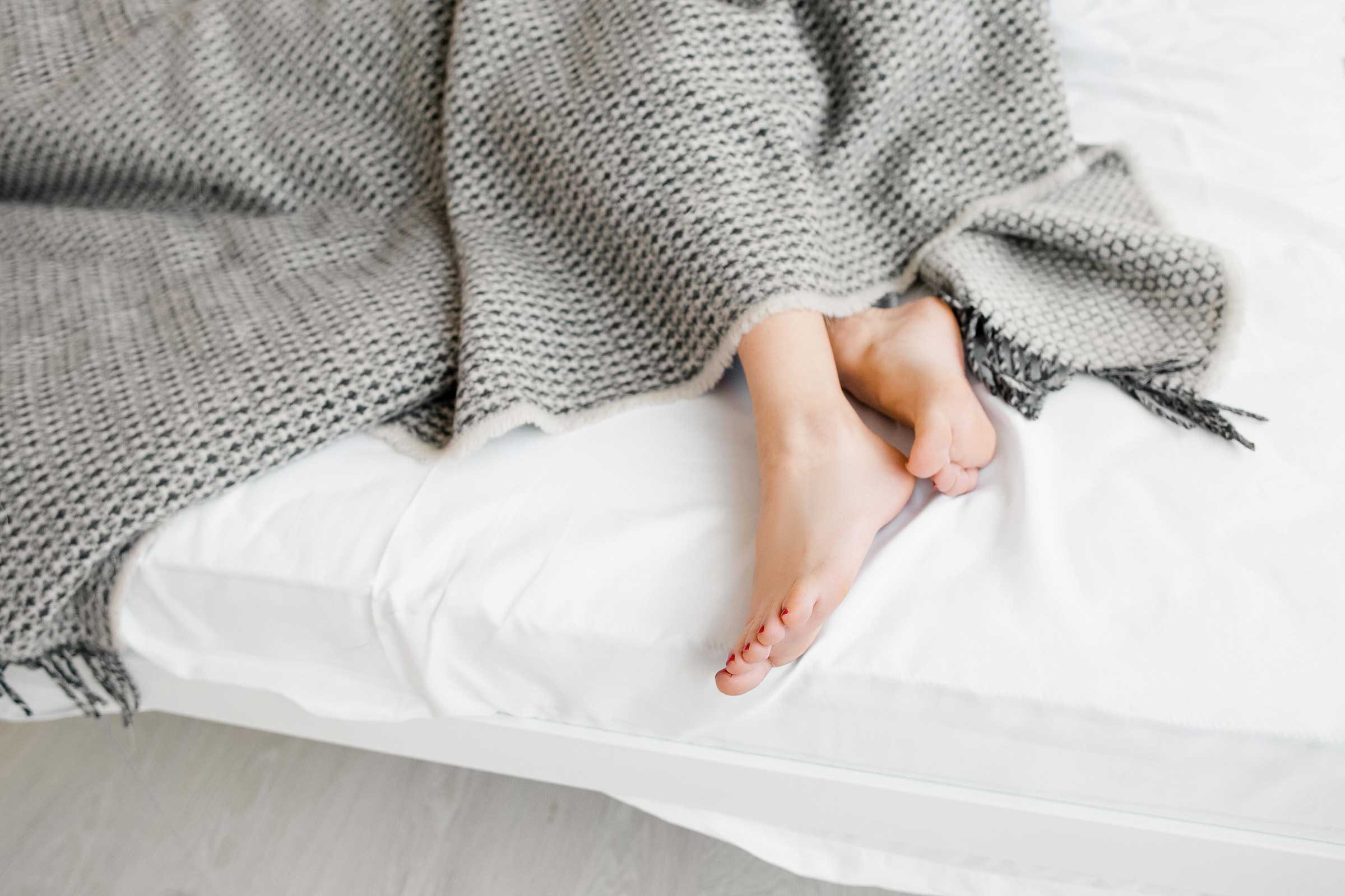 A person's feet poking out from underneath a gray blanket.