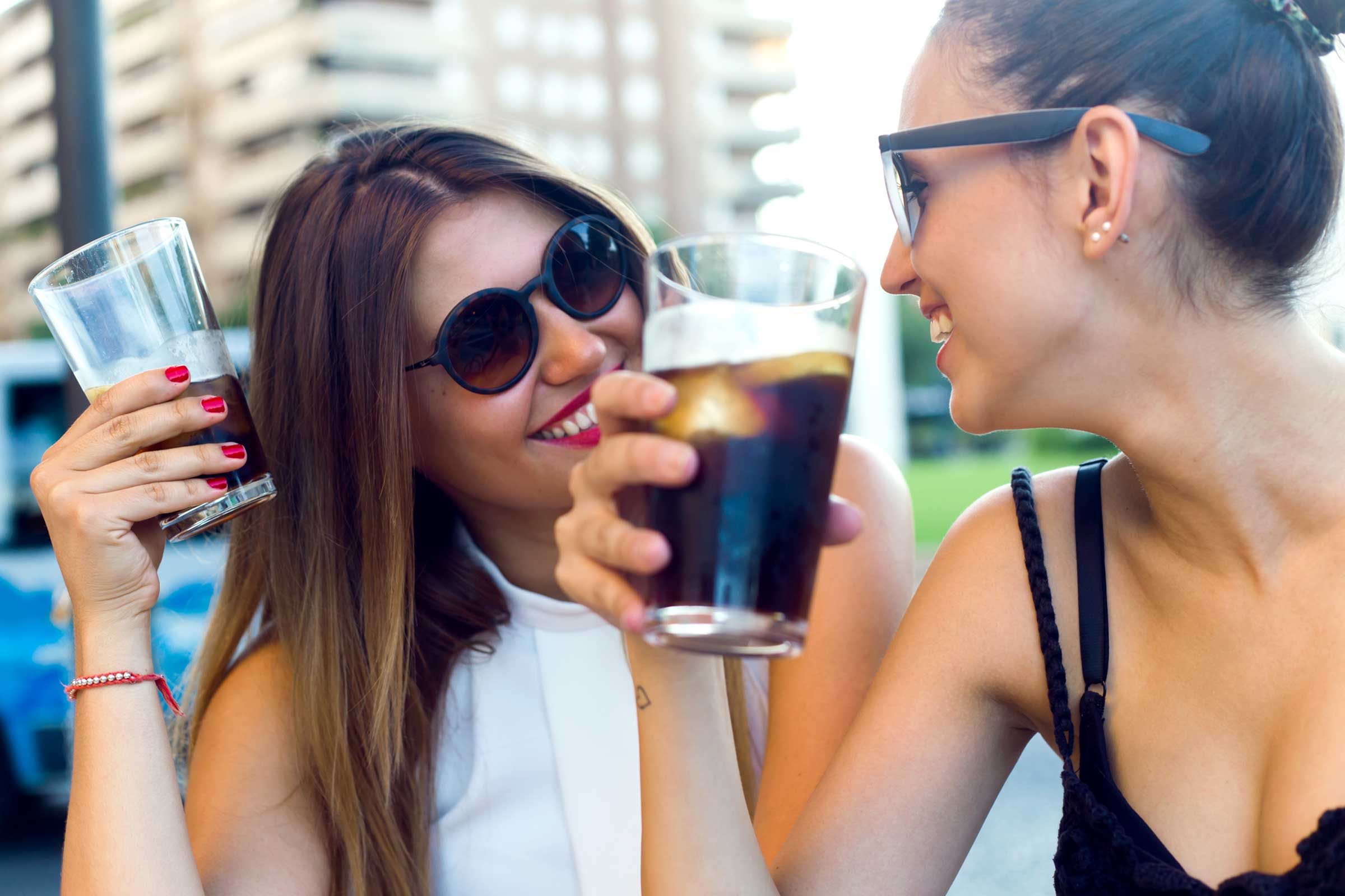 two woman holding glasses of cola 