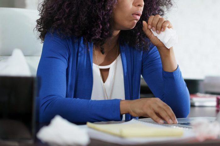 Woman in a blue cardigan coughing into a tissue.