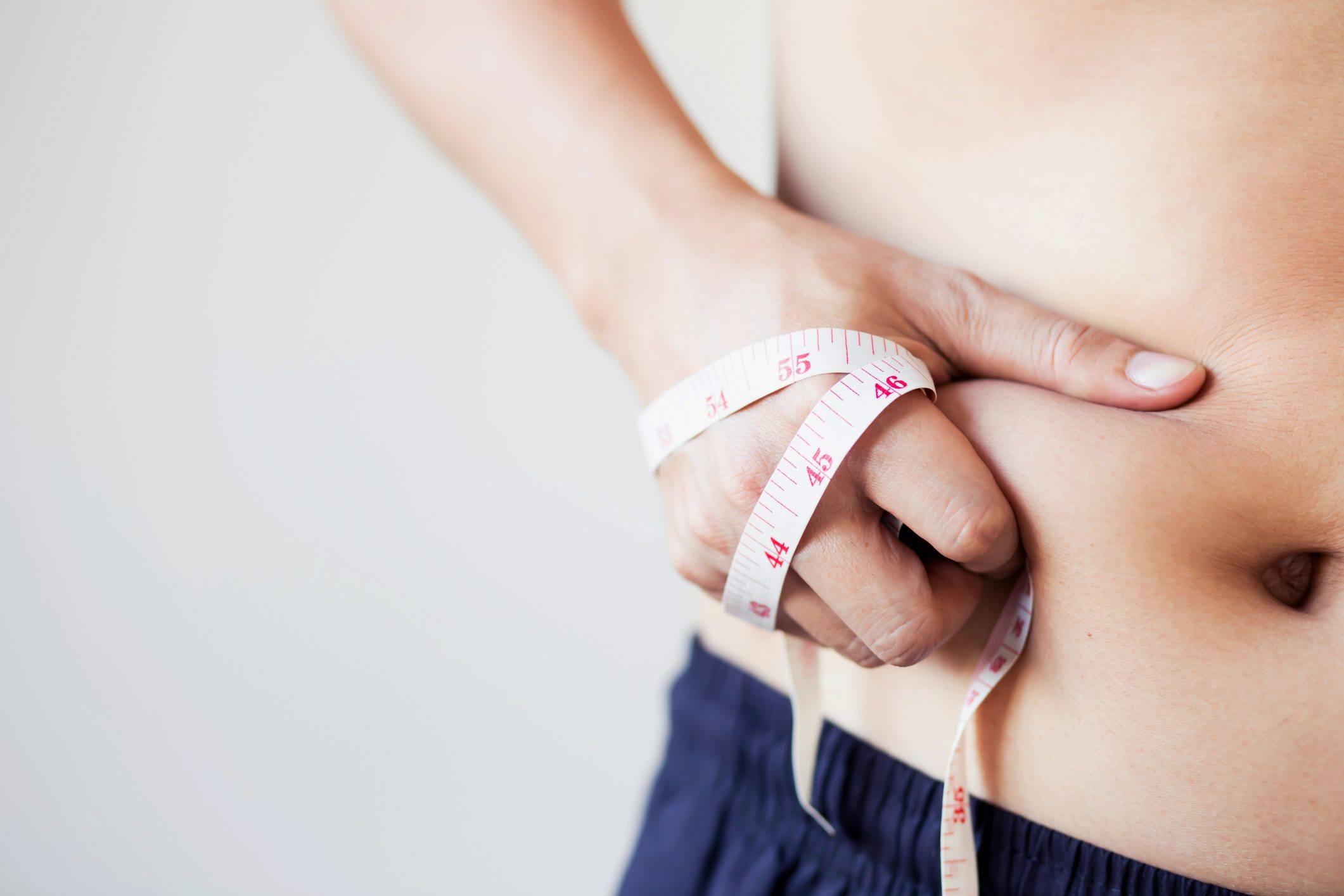close up of man's stomach and hand holding measuring tape