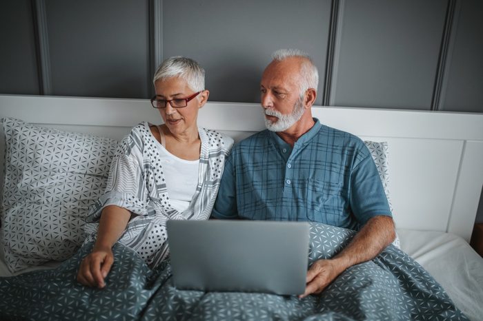 couple in bed talking and using laptop