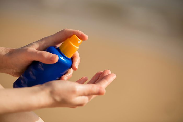 Person applying spray tan sunscreen to her hands.