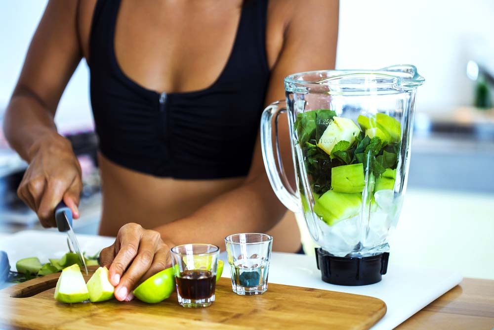 Woman in workout garb slicing apples for a smoothie.