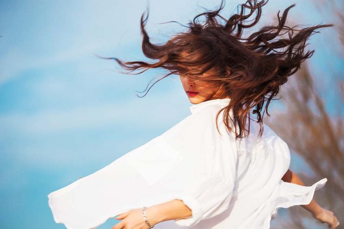 A woman spinning in a circle outdoor with her hair in the wind.