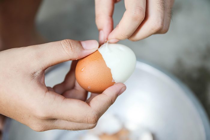 Hands peeling shell from a hard-boiled egg.