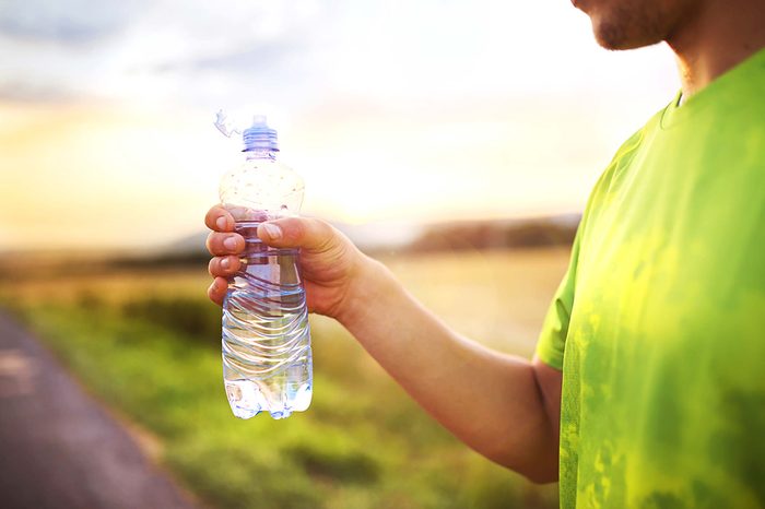 Man wearing a green shirt holding a plastic water bottle in his right hand.