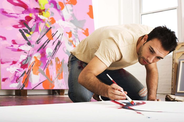 Male painter kneeling and painting canvas