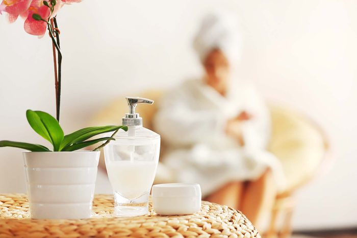 A woman sitting on a chair at the spa with a lotion and orchard in the foreground.
