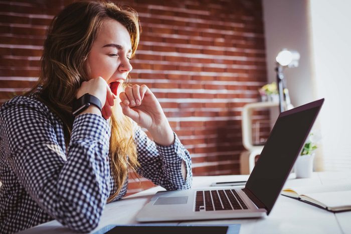 woman yawning in front of a laptop computer