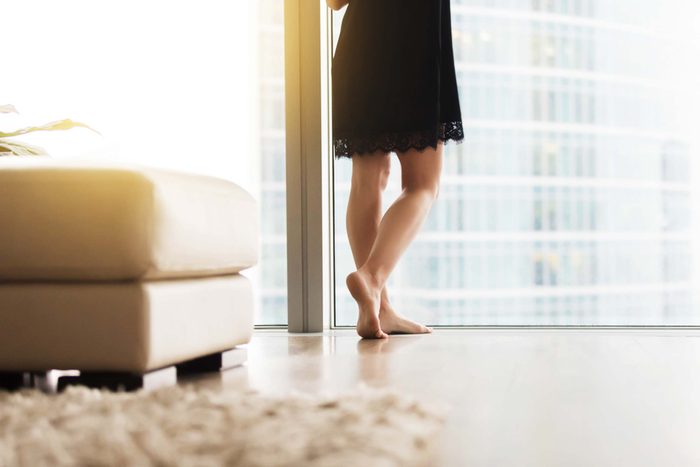 anonymous woman standing near the window of an apartment