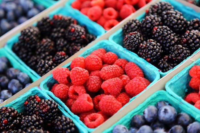 trays of raspberries, blackberries, and blueberries at a farmers market