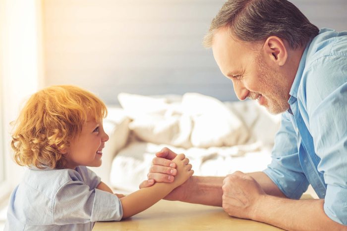 grandfather and grandson laugh as they arm wrestle