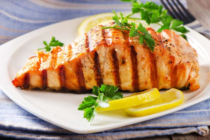grilled salmon on a white plate with lemon and garnish