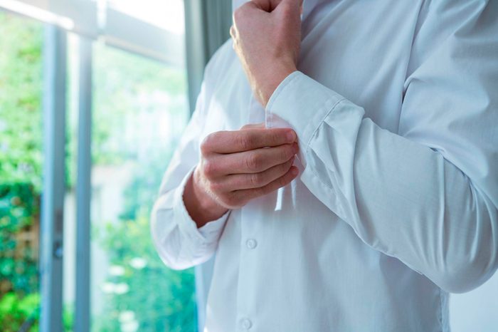 man buttoning sleeve of white shirt in morning sun