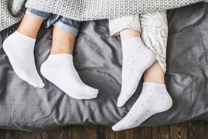 two sets of sock-clad feet peeking out of the bed covers