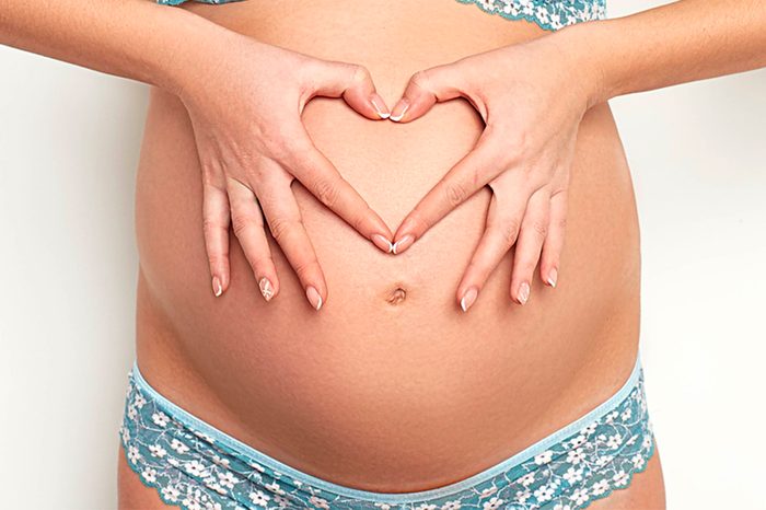 pregnant woman's bare belly; she's making a heart out of her fingers over her belly