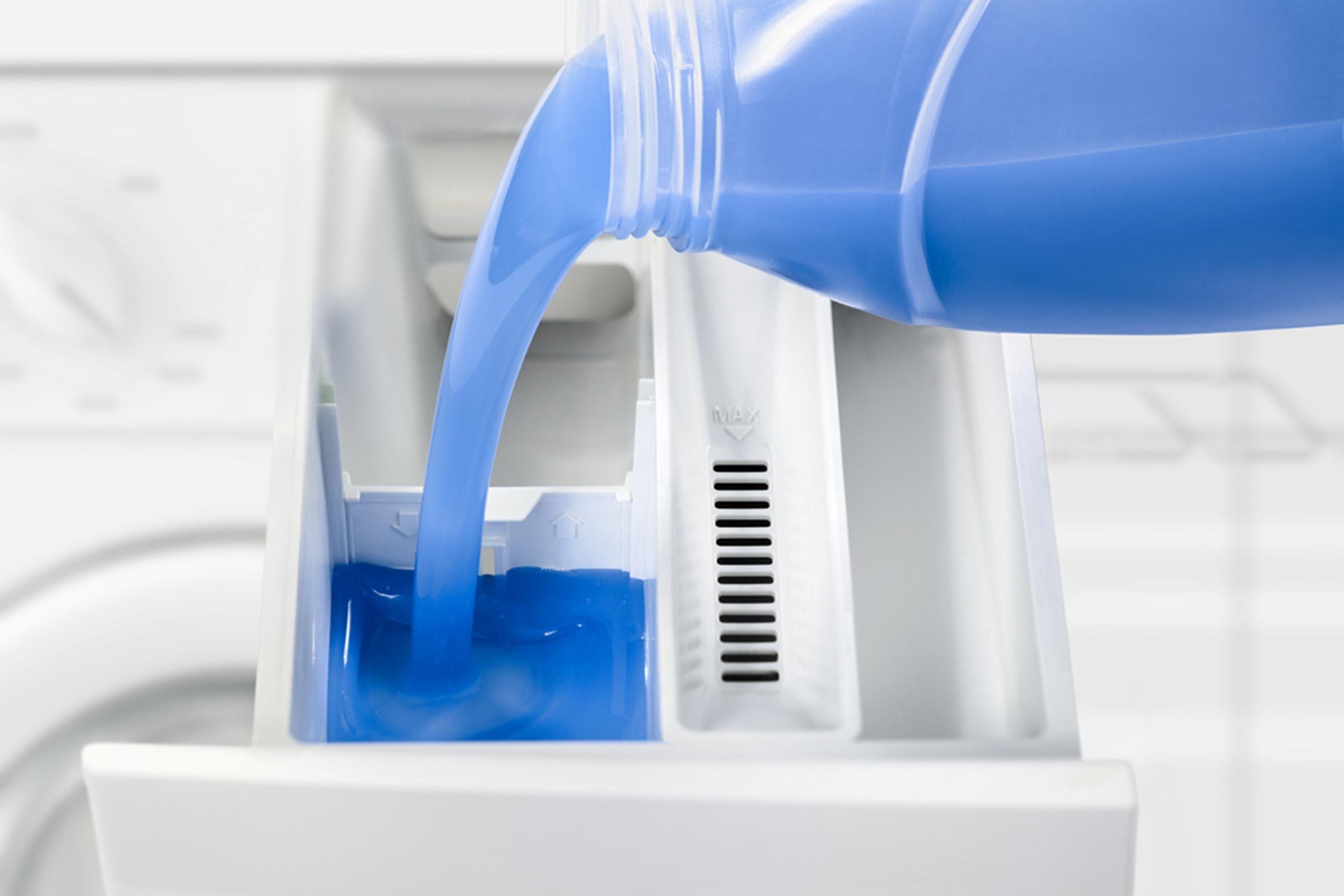 Washing machine dispenser being filled with liquid detergent.