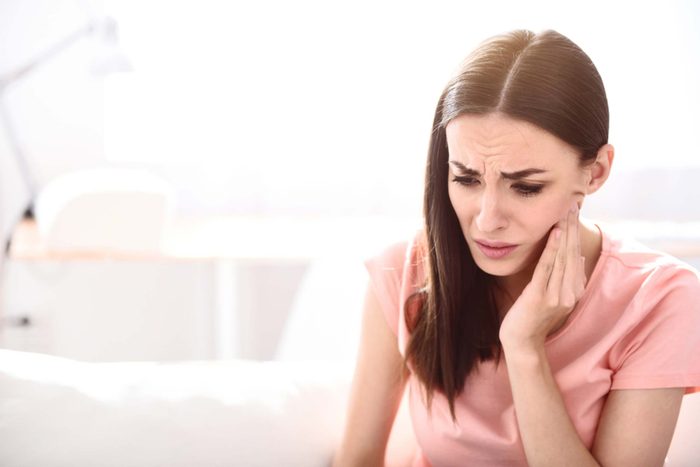 Woman with furrowed brow holding her jaw.