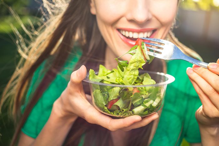 Smiling woman eating a salad with a fork.