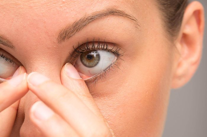 A woman with hazel eyes rubbing her eyes.