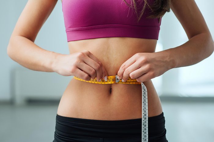 Woman measuring her stomach with a tape measure.