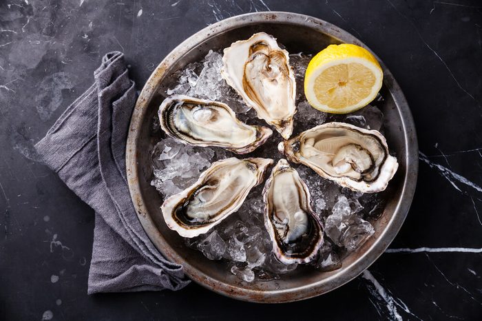 Opened Oysters on metal plate with ice and lemon on dark marble background
