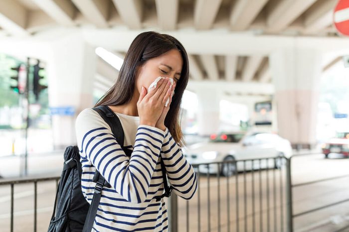 Asian Woman sneezing in into a tissue