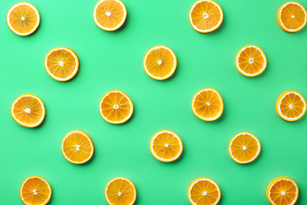 Colorful fruit pattern of fresh orange slices on green background. From top view