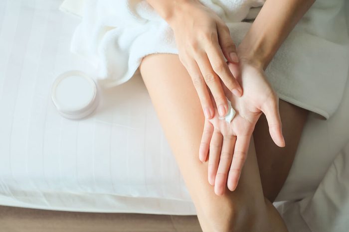 Asian woman sitting on a bed and applying cream on her hand.