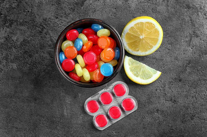 Different cough drops with lemon on grey background.