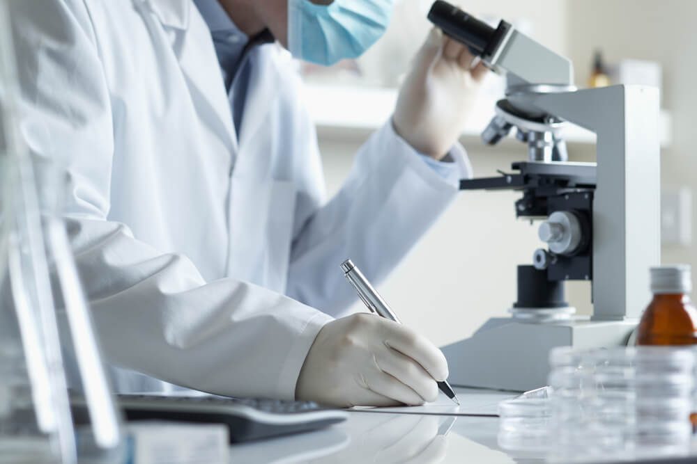 Scientist conducting research taking notes whilst looking through microscope selective focus