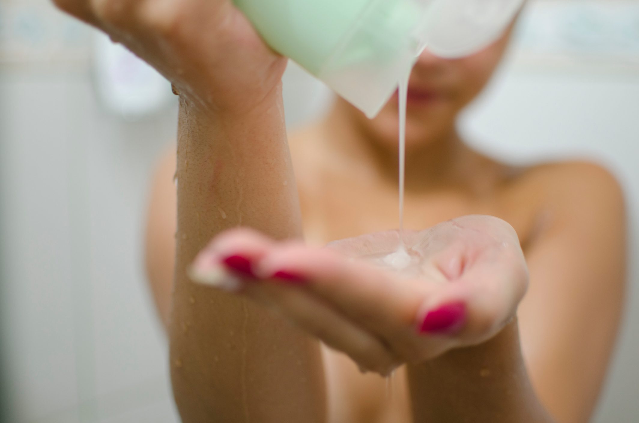 woman pouring shampoo into hand in shower