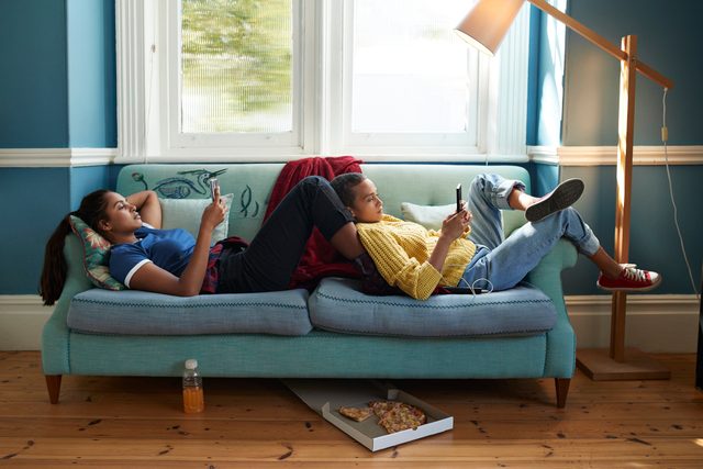 two young women relaxing on couch while looking at smartphones